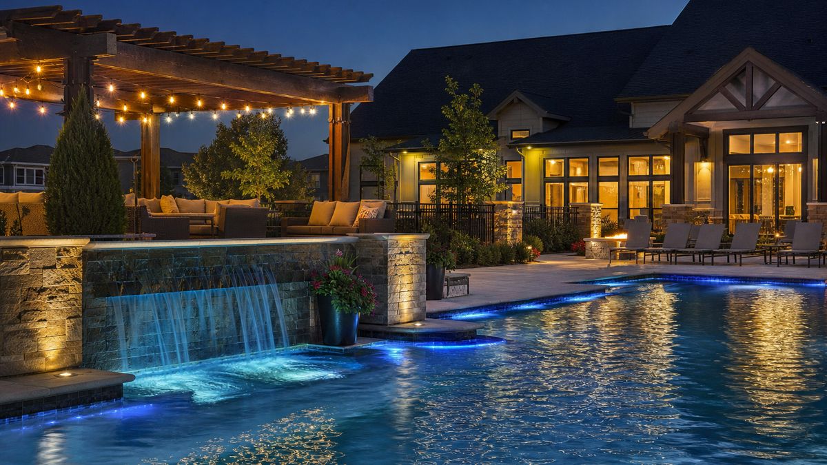 HOA community pool deck with warm lighting, pergola and lit water feature in the evening